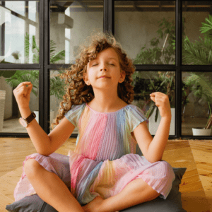 Petite fille en robe colorée méditant assise sur un coussin dans une posture zen